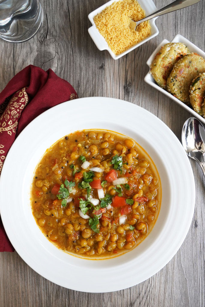 Top view: Ragda garnished with tomatoes, cilantro, and onion in a white plate.