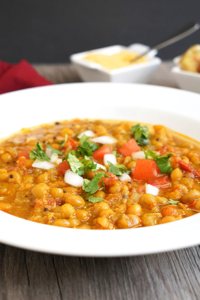 Ragda garnished with tomatoes, cilantro, and onion in a white plate.