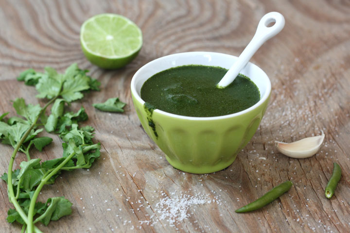 Green chutney in a green colored bowl with fresh ingredients surrounding the bowl.