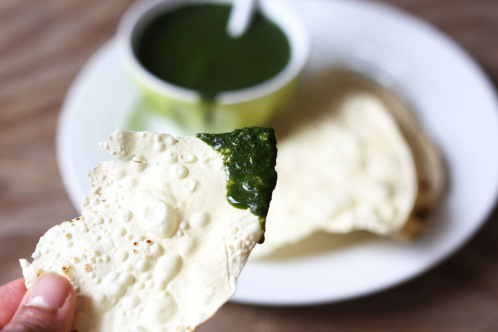 Pappadum being dipped into cilantro chutney.