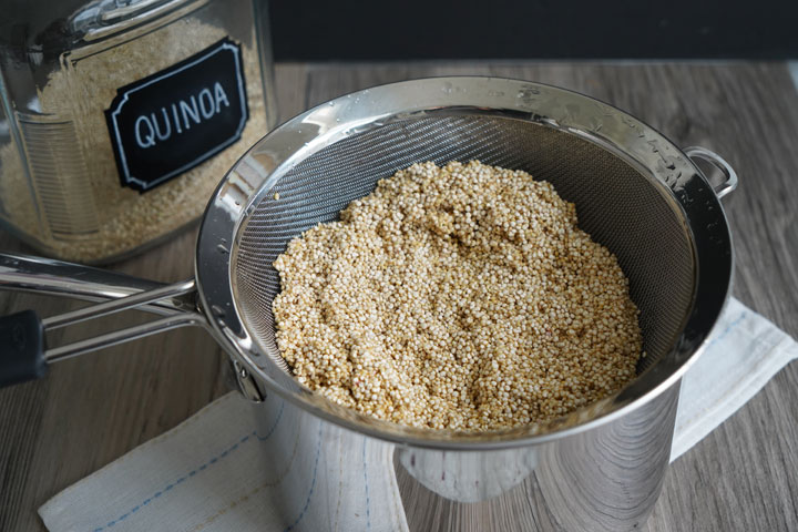 Rinsed quinoa in a strainer, draining over a pot.