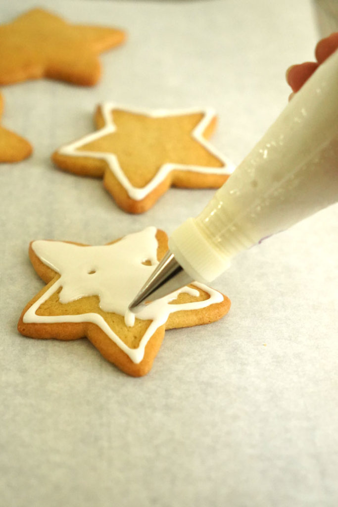 Star shaped cookie being decorated with white royal icing.