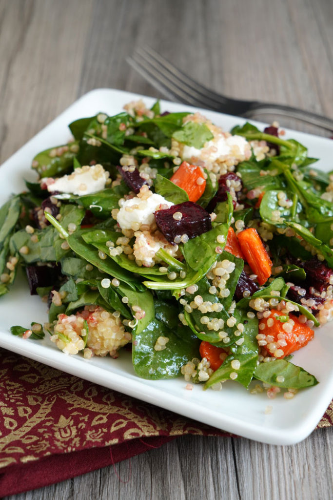 Spinach, roasted beets and carrots, quinoa salad on a white plate.