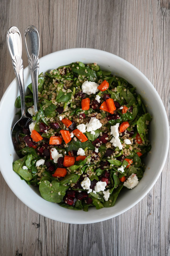 Spinach, roasted beets and carrots, quinoa salad in a large bowl.