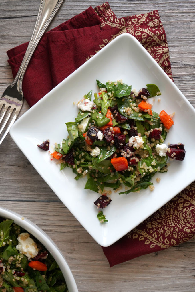 Spinach, roasted beets and carrots, quinoa salad on a white plate.