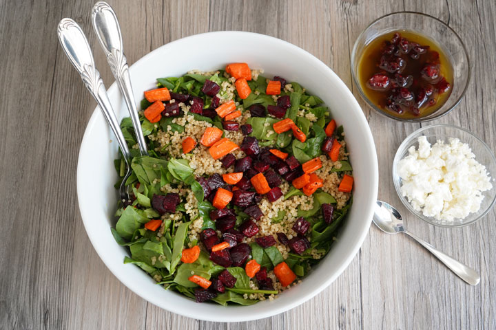 Spinach, roasted beets and carrots, quinoa salad being mixed in a large bowl.