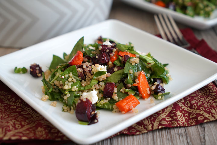 Spinach, roasted beets and carrots, quinoa salad on a white plate.