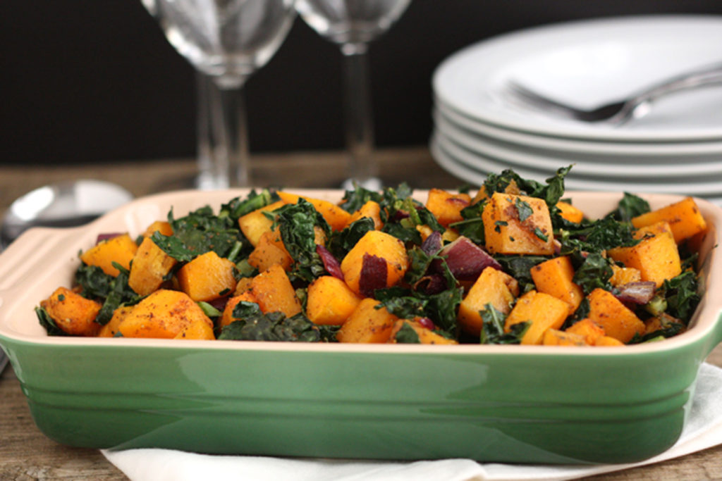 Spicy butternut squash with kale and red onion in a green serving dish.