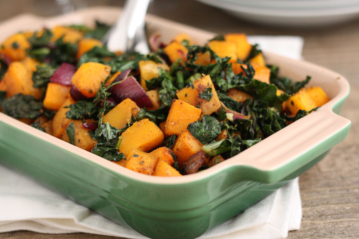 Spicy butternut squash with kale and red onion in a green serving dish.