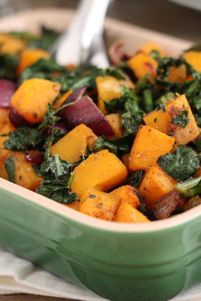 Spicy butternut squash with kale and red onion in a green serving dish.