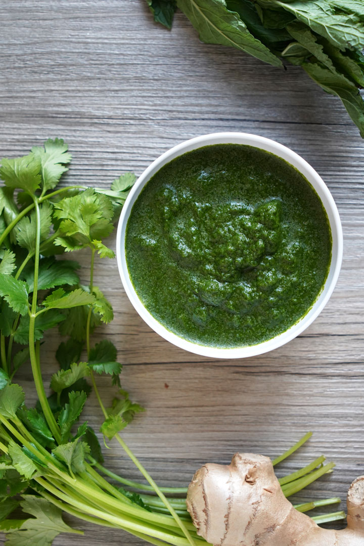 Top view of cilantro mint chutney in white bowl with fresh cilantro and ginger on the side.