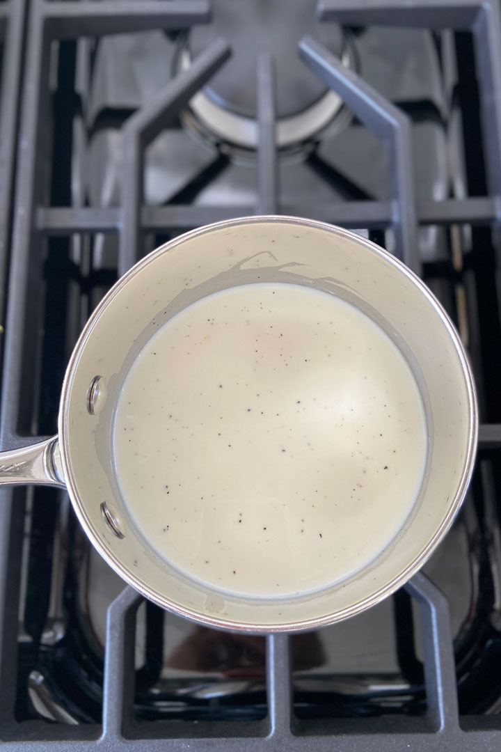 Milk, cream, sugar and vanilla bean being heated over a gas burner.