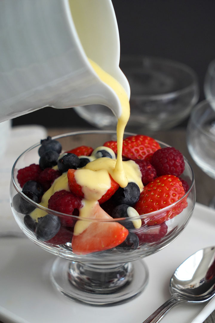 Custard sauce being poured over fresh berries. 