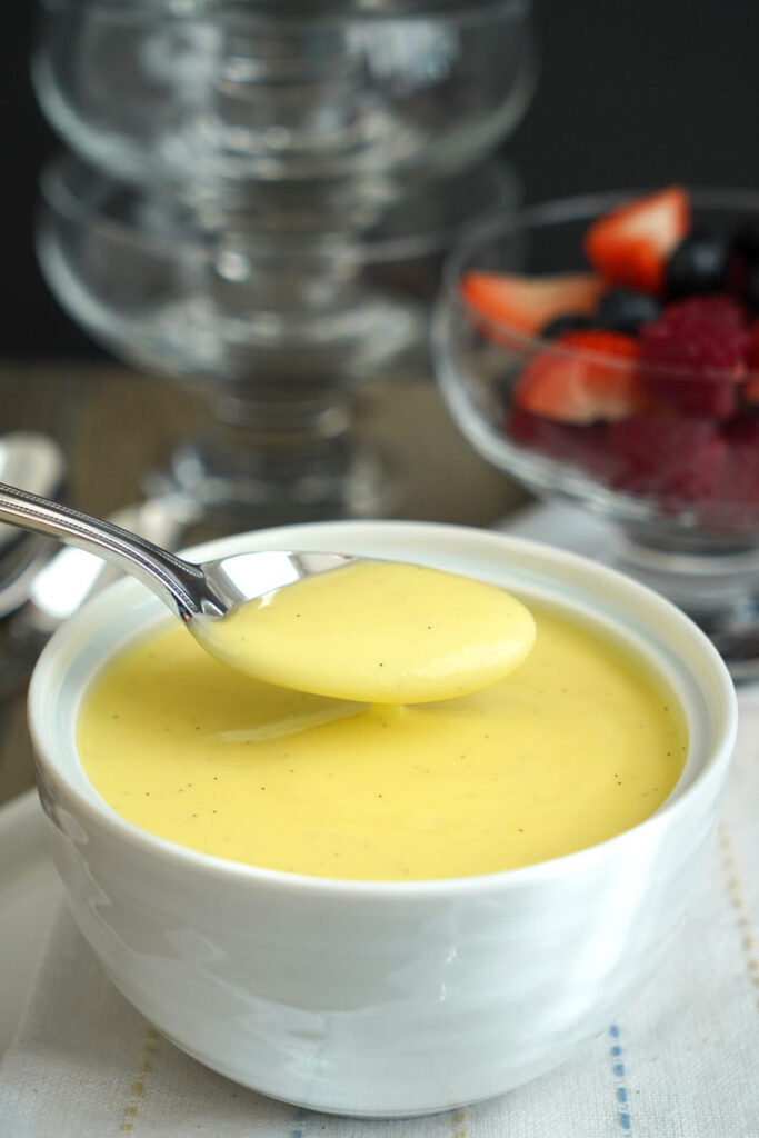 Vanilla sauce being spooned out of white bowl.