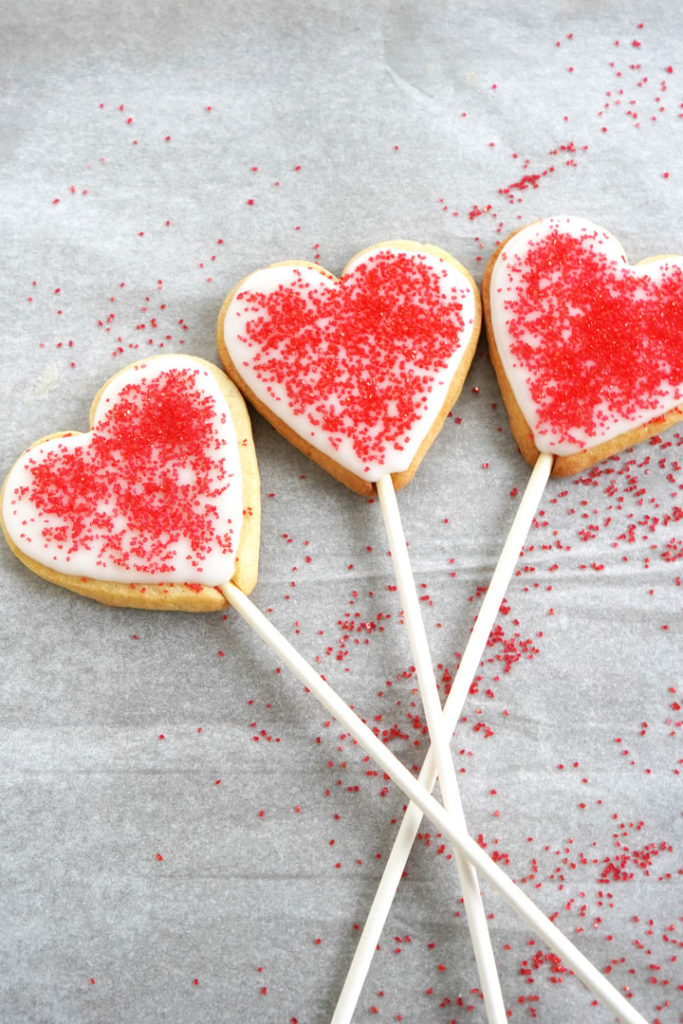 Heart shaped sugar cookies with red sugar crystals on a stick.