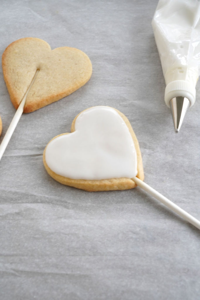 Baked heart shaped sugar cookie dough attached to a stick with icing.