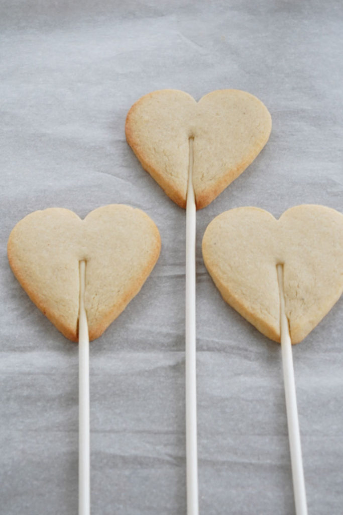 Baked heart shaped sugar cookie dough attached to a stick.