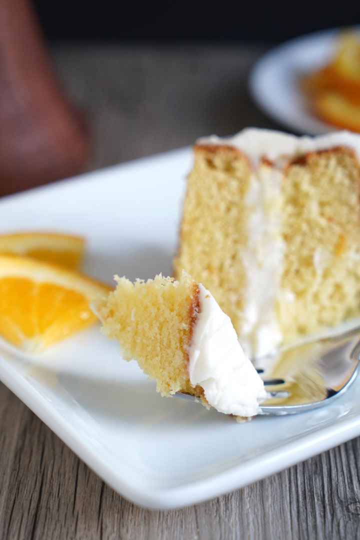 Orange flavored cake with cream cheese frosting on a fork with slice in the background.