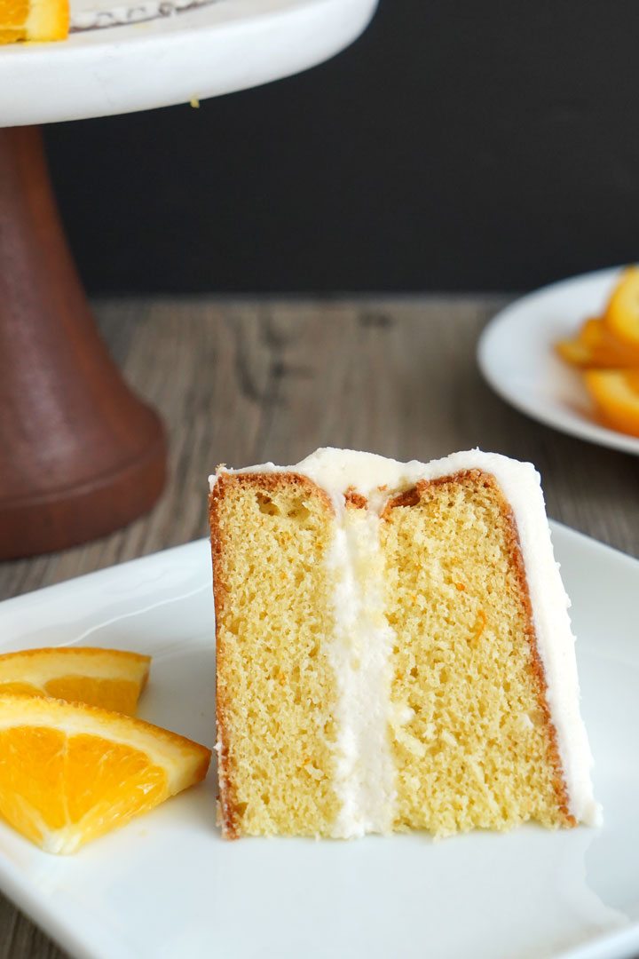 A slice of cake on a white plate. Orange slices on the side.