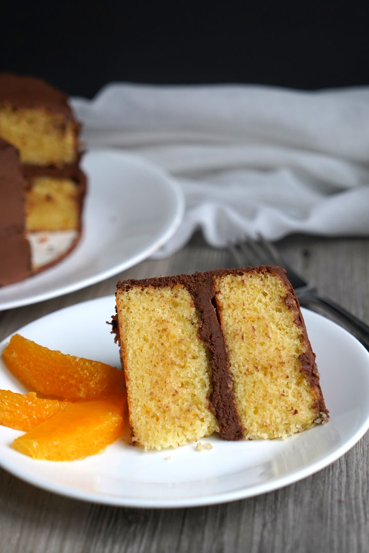 Chocolate frosted orange flavored cake slice on a white plate with segmented orange slices on the side.