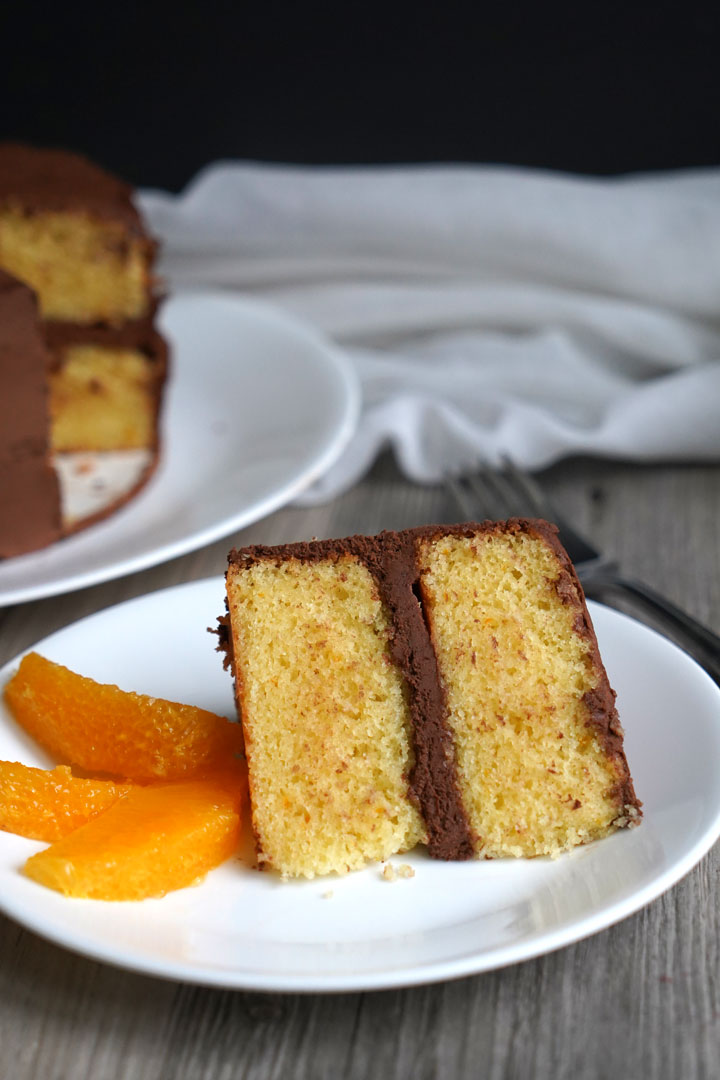 Chocolate frosted orange flavored cake slice on a white plate with segmented orange slices on the side. 