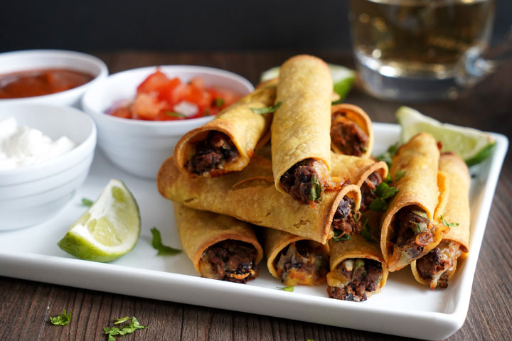 Bean and cheese taquito stacked on a white plate with sides.