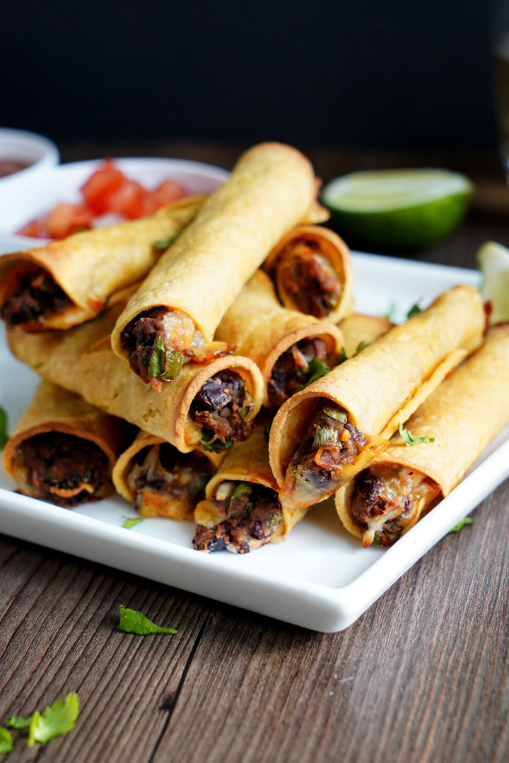 Bean and cheese taquitos stacked on a white plate