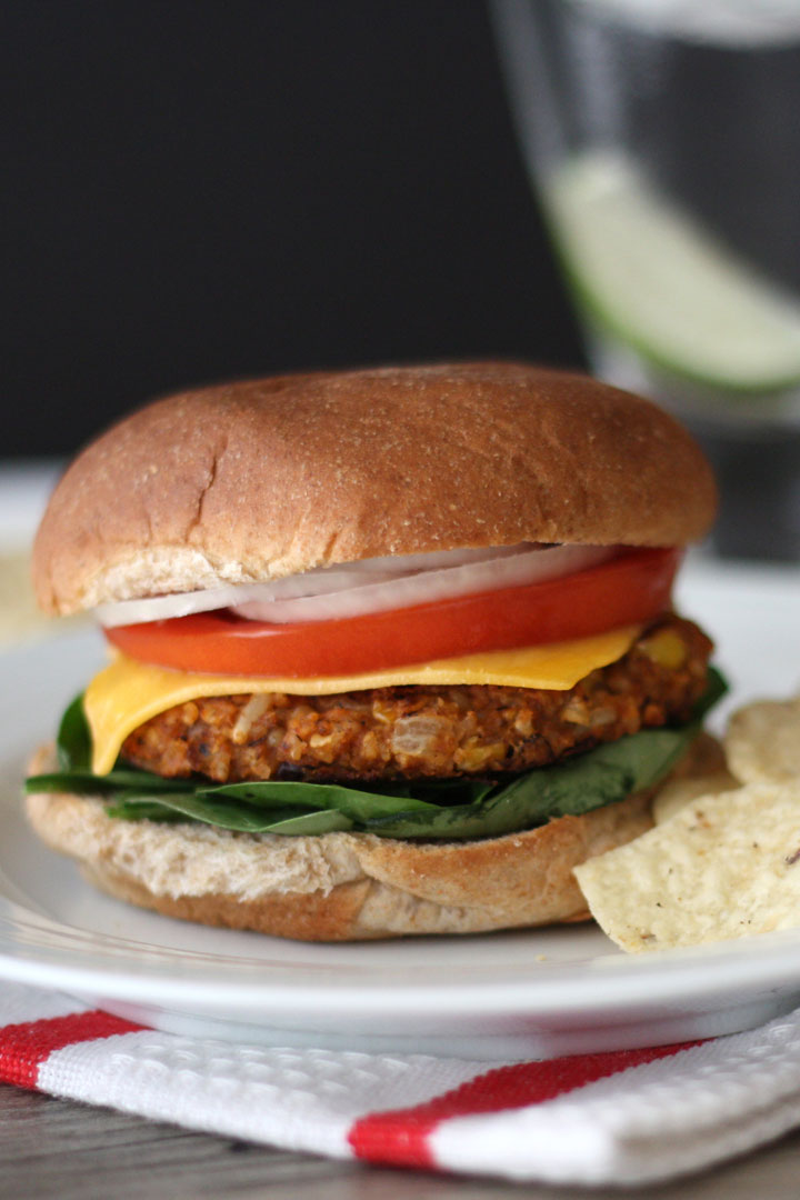 Black bean burger with spinach, cheese, tomato and onion with a side of tortilla chips in a white plate. 