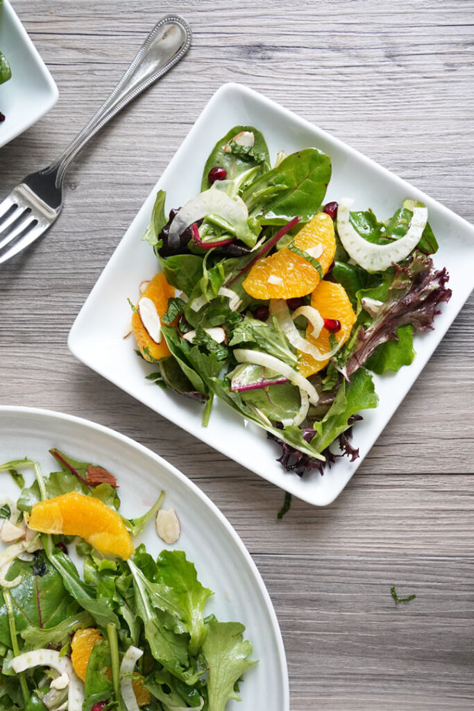 Orange fennel salad in plate with serving platter in background.