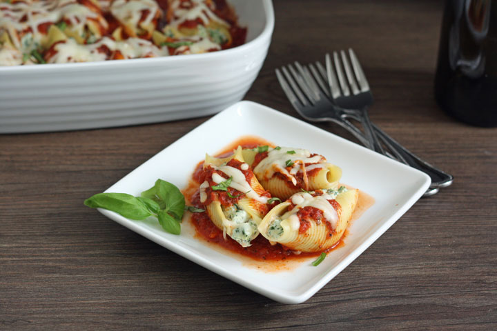 3 stuffed shells on white plate with forks and casserole dish in background.