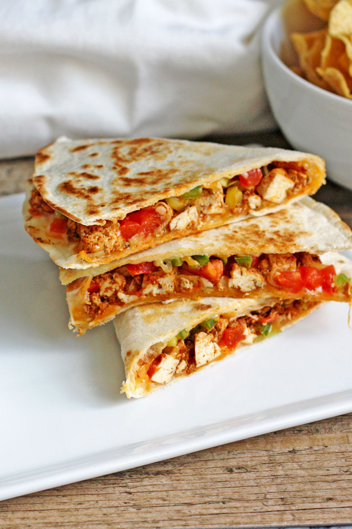 Close up view of 3 quesadilla pieces stacked on a white plate.