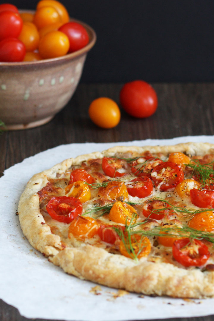 Half of tomato tart on parchment paper with grape tomatoes in back ground. 