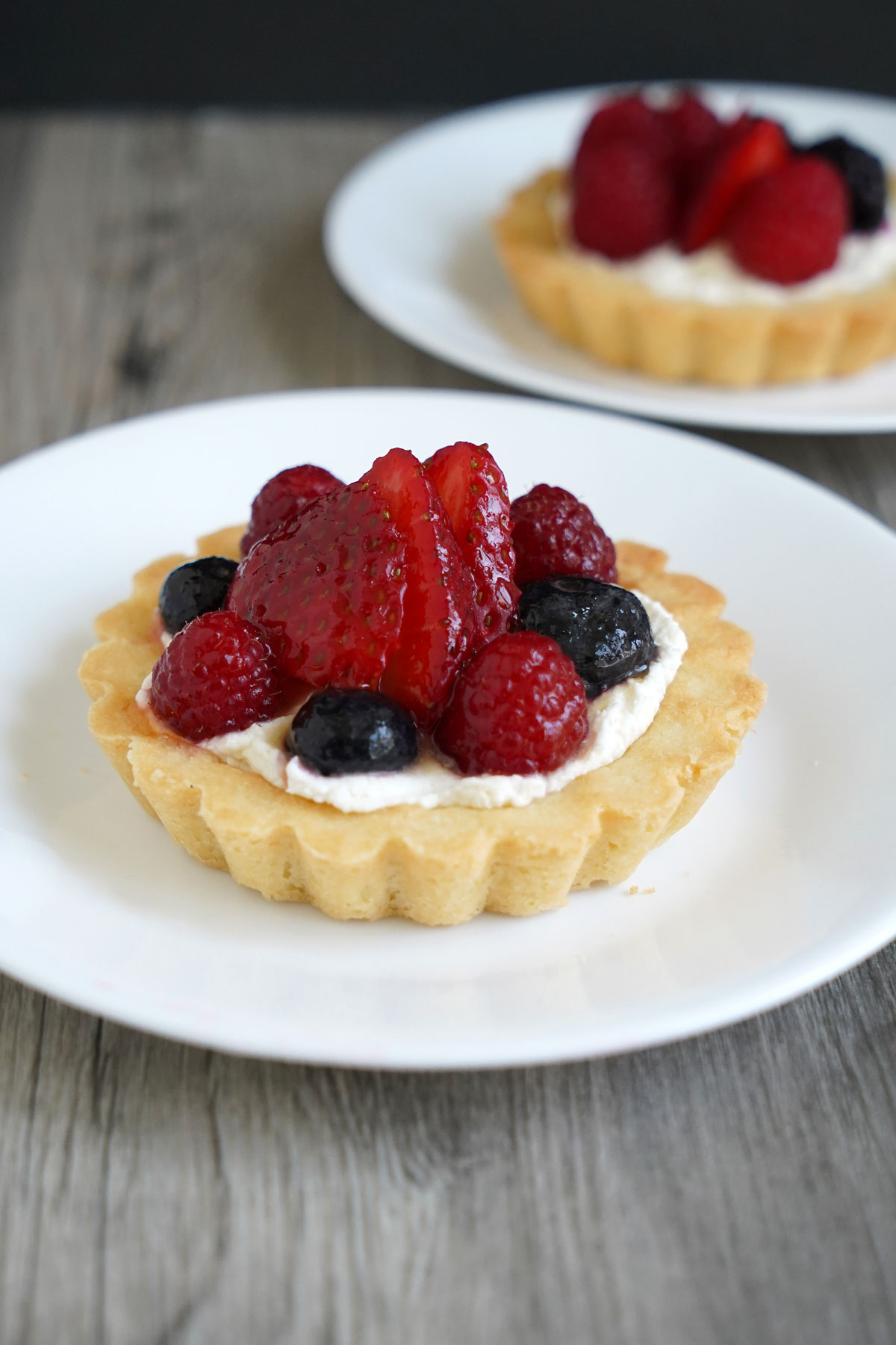 A fruit tart with strawberries, raspberries and blueberries on a white plate.