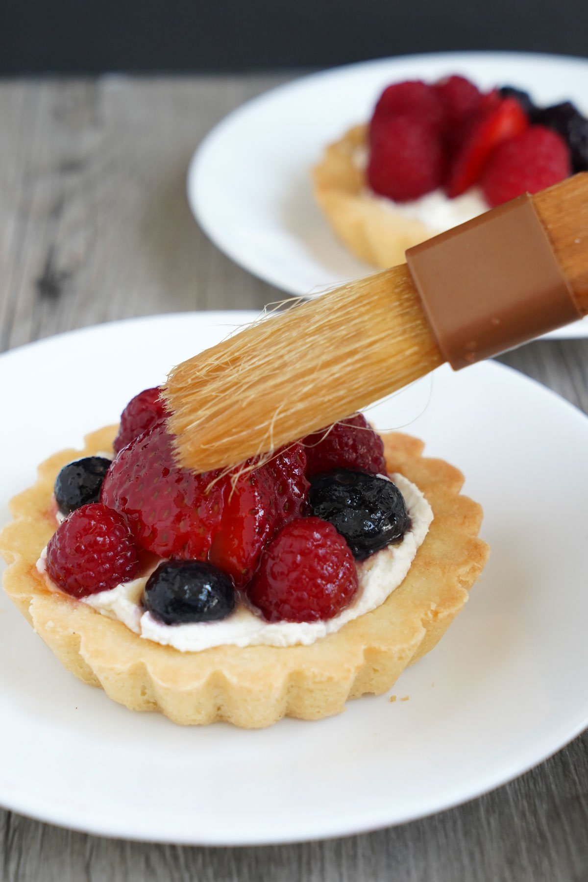 A shiny fruit glaze being brushed onto a fruit tart.