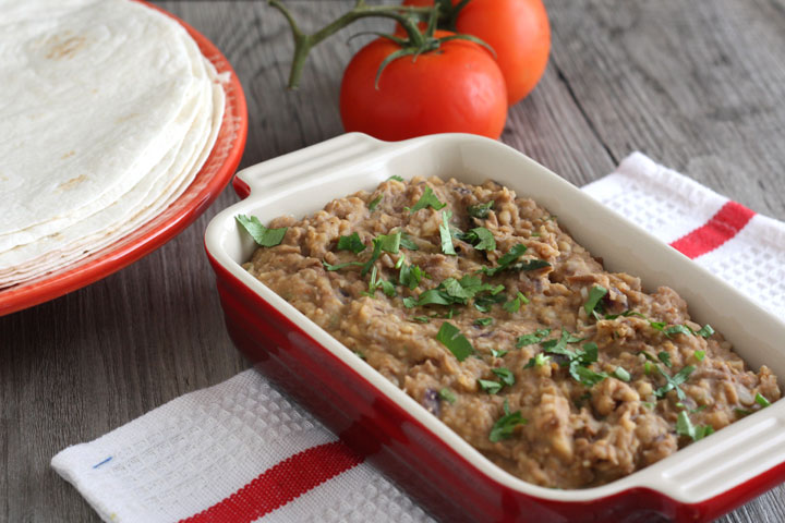 Tortillas, refried beans and tomatoes on a table.