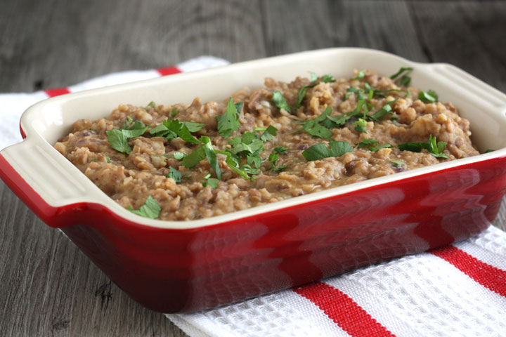 Refried beans in red serving dish, garnished with cilantro.