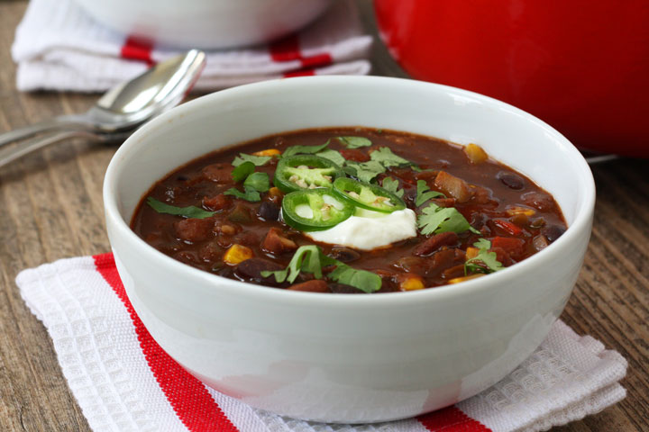 Three bean vegetarian chili in a white bowl topped with jalapenos and sour cream.