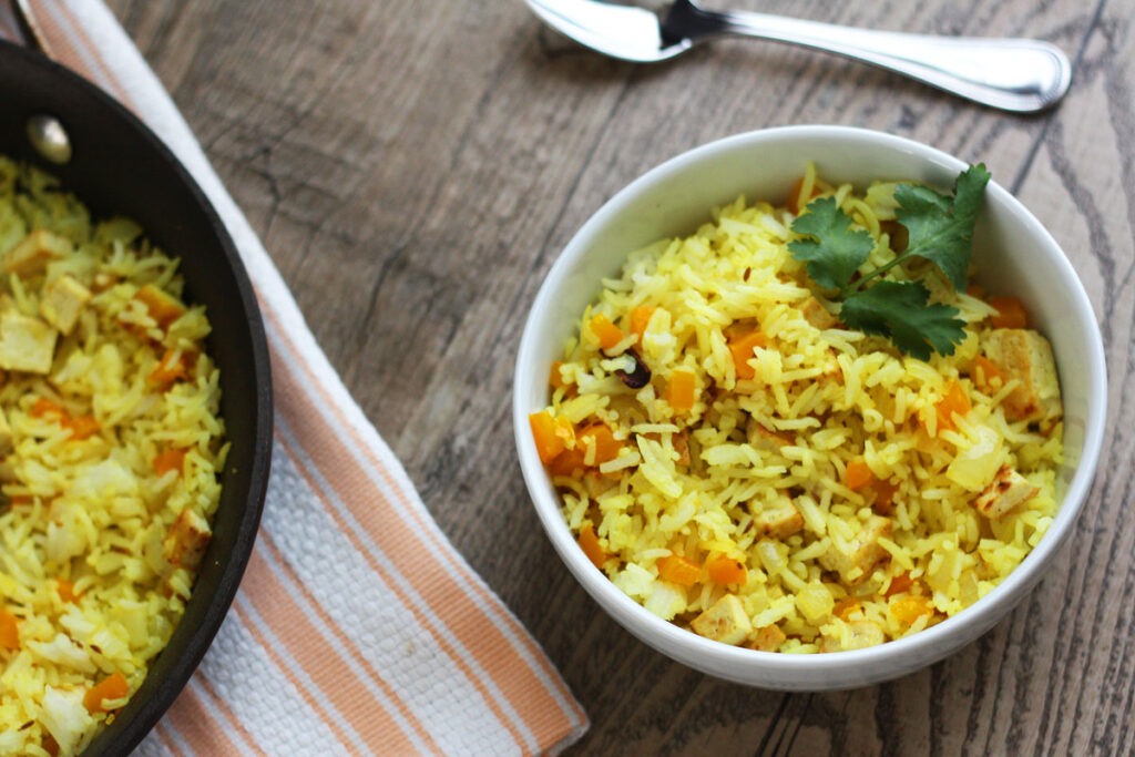 Top view of fried rice in bowl with pan of rice on orange towl.
