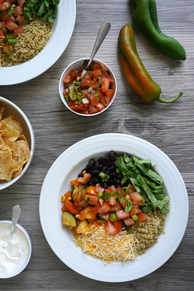 Bird's eye view of quinoa bowl on table with sides of fresh salsa, chips, and sour cream.