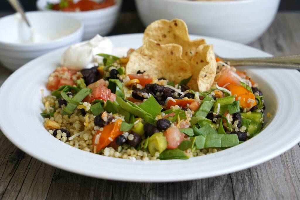 Quinoa Burrito Bowl after mixing ingredients, with tortilla chip and sour cream garnish.