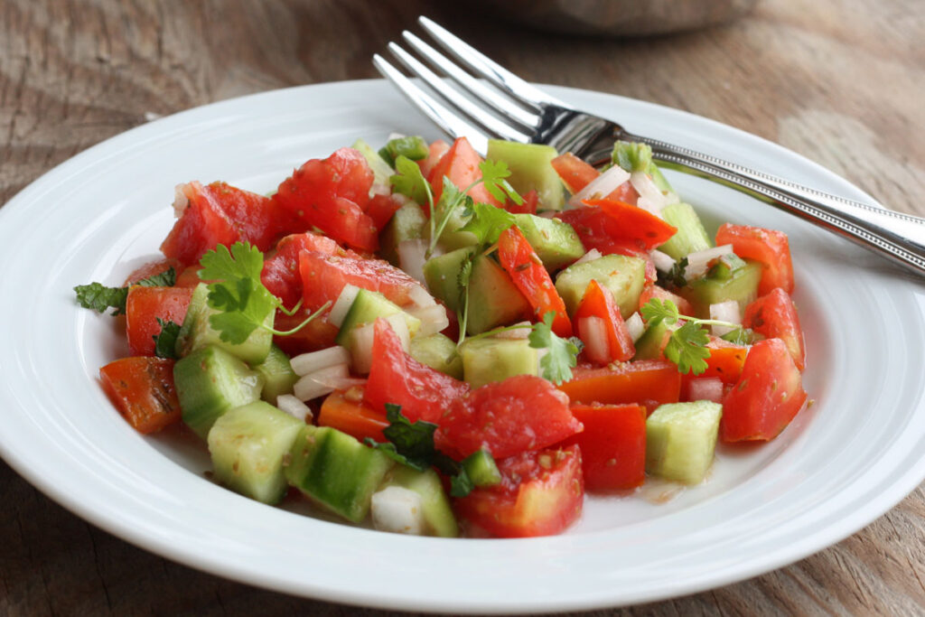 Cucumber tomato salad in a white plate with fork.