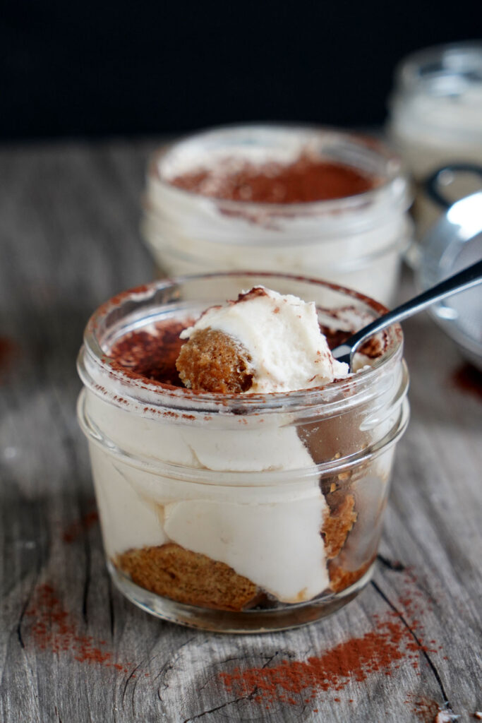 Tiramisu in a jar with spoonful on top.