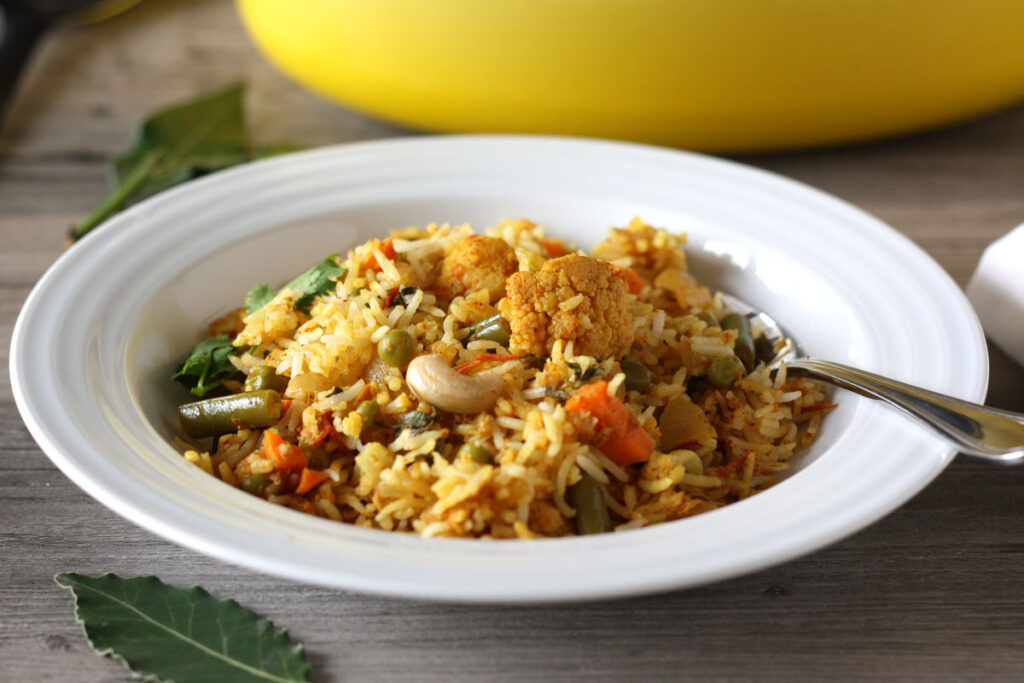 Biryani in a white dish with spoon. Pot in background.