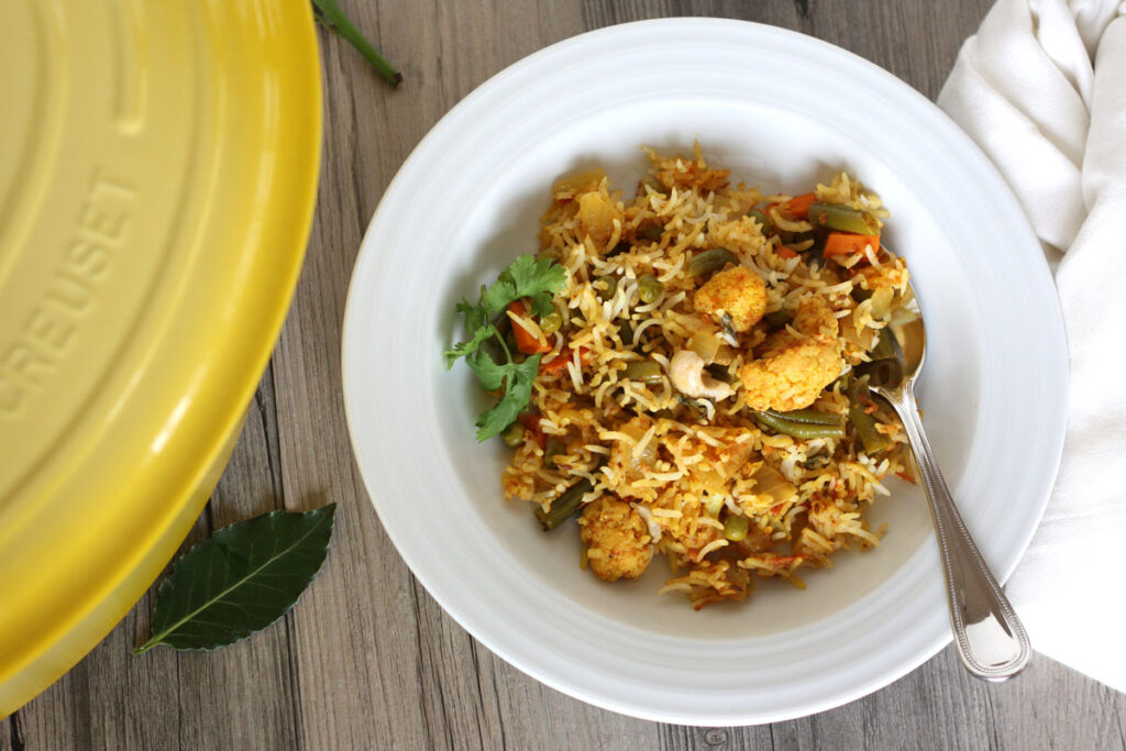 Top view of biryani in a white dish with spoon and napkin.