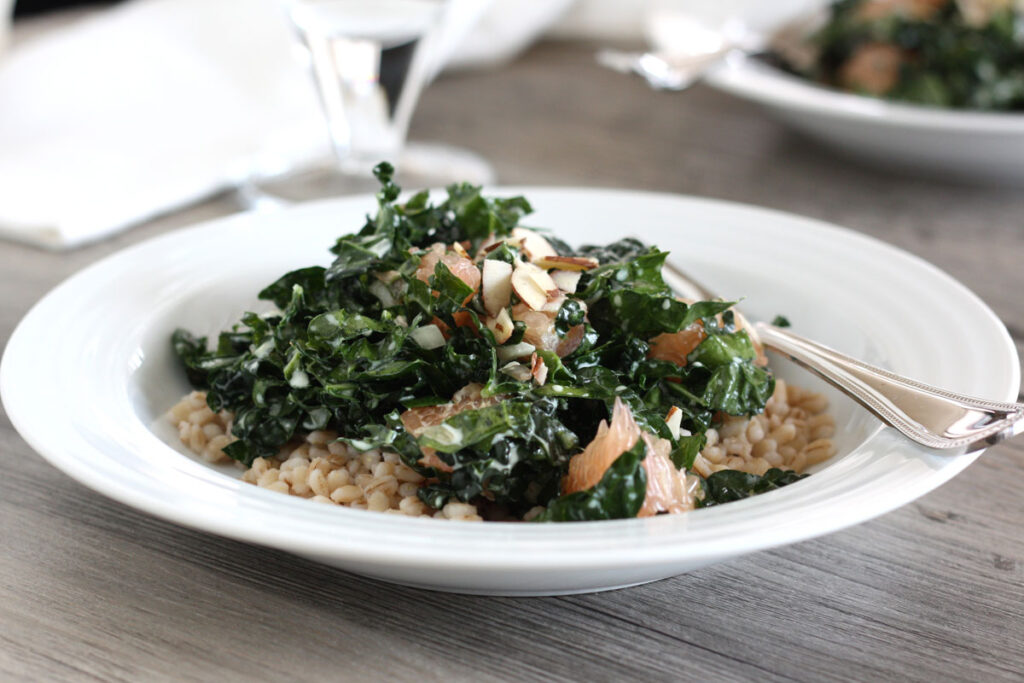 Kale and barley salad in a white plate with spoon. 