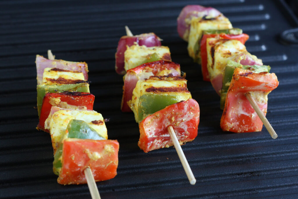 Vegetable and paneer on skewers on grill.