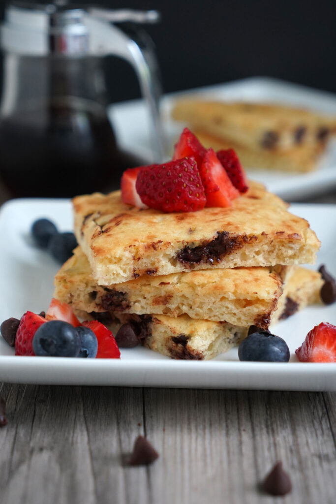 Three rectangular pancakes stacked in a white plate with fresh berry toppings. Syrup on the side.