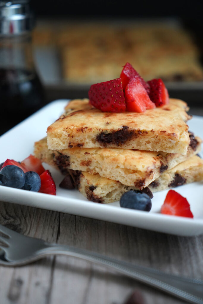 Sheet pan chocolate chip pancakes with berry toppings with in a white plate with fork.