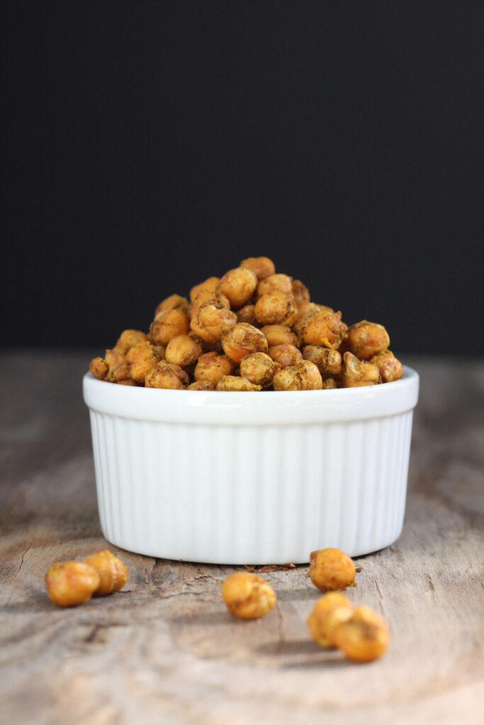Spicy roasted chickpeas in white bowl with some chickpeas out side bowl.