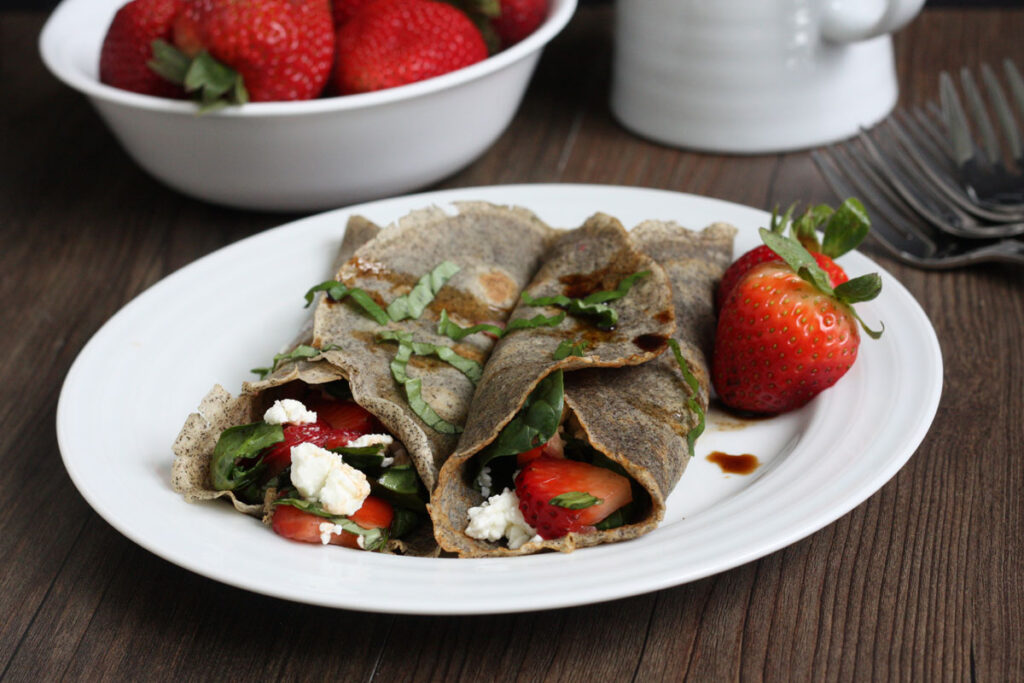 Two buckwheat crepes with strawberry spinach filling on white plate. 